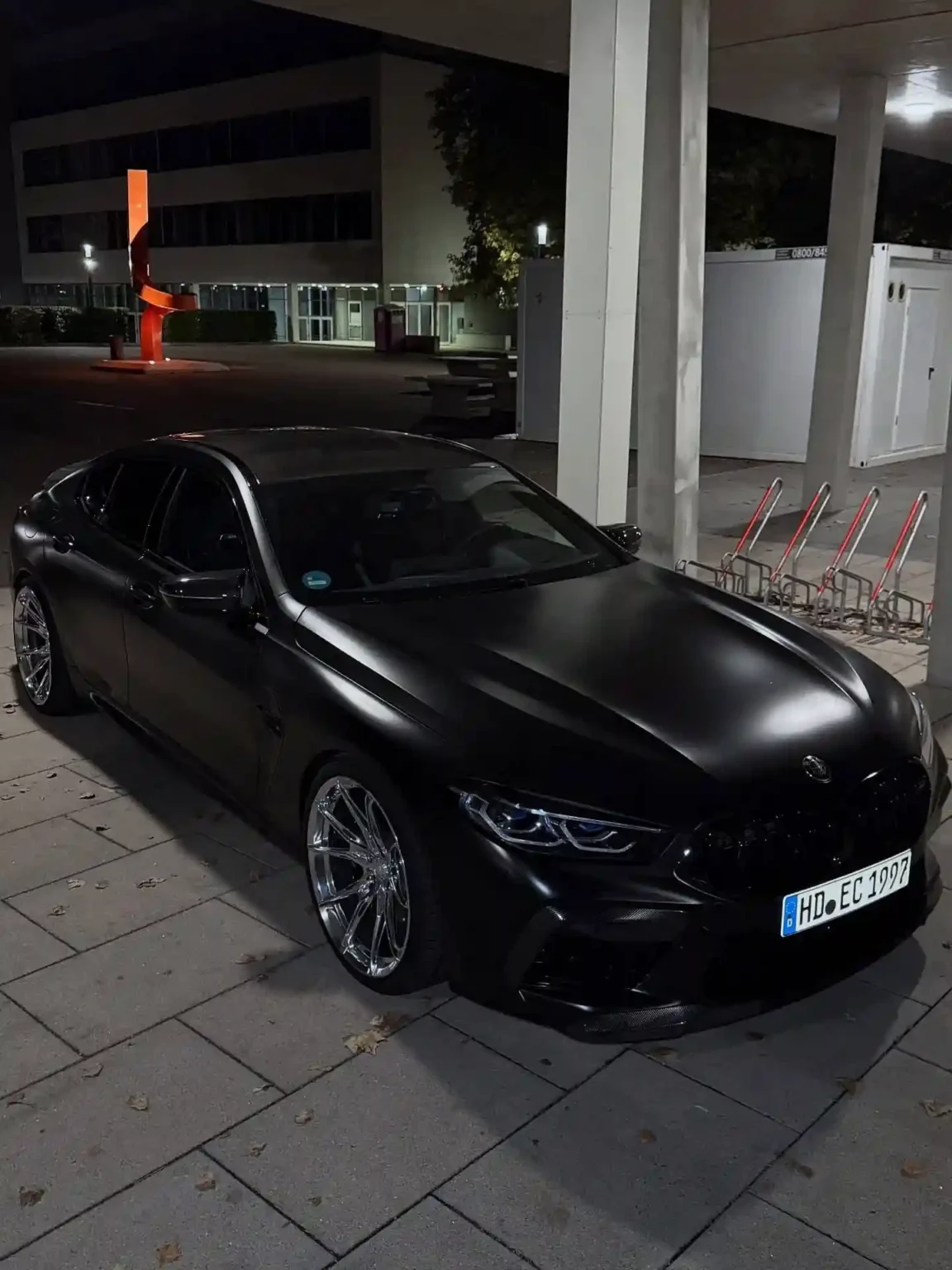 A matte black luxury BMW i5 sedan parked outside a hotel, waiting to pick up a passenger.
