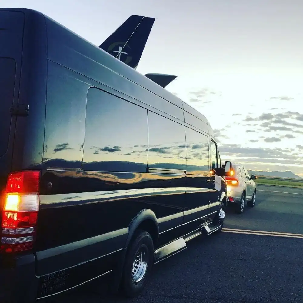 A black luxury Mercedes Sprinter parked beside a private jet, ready to drop off a passenger.
