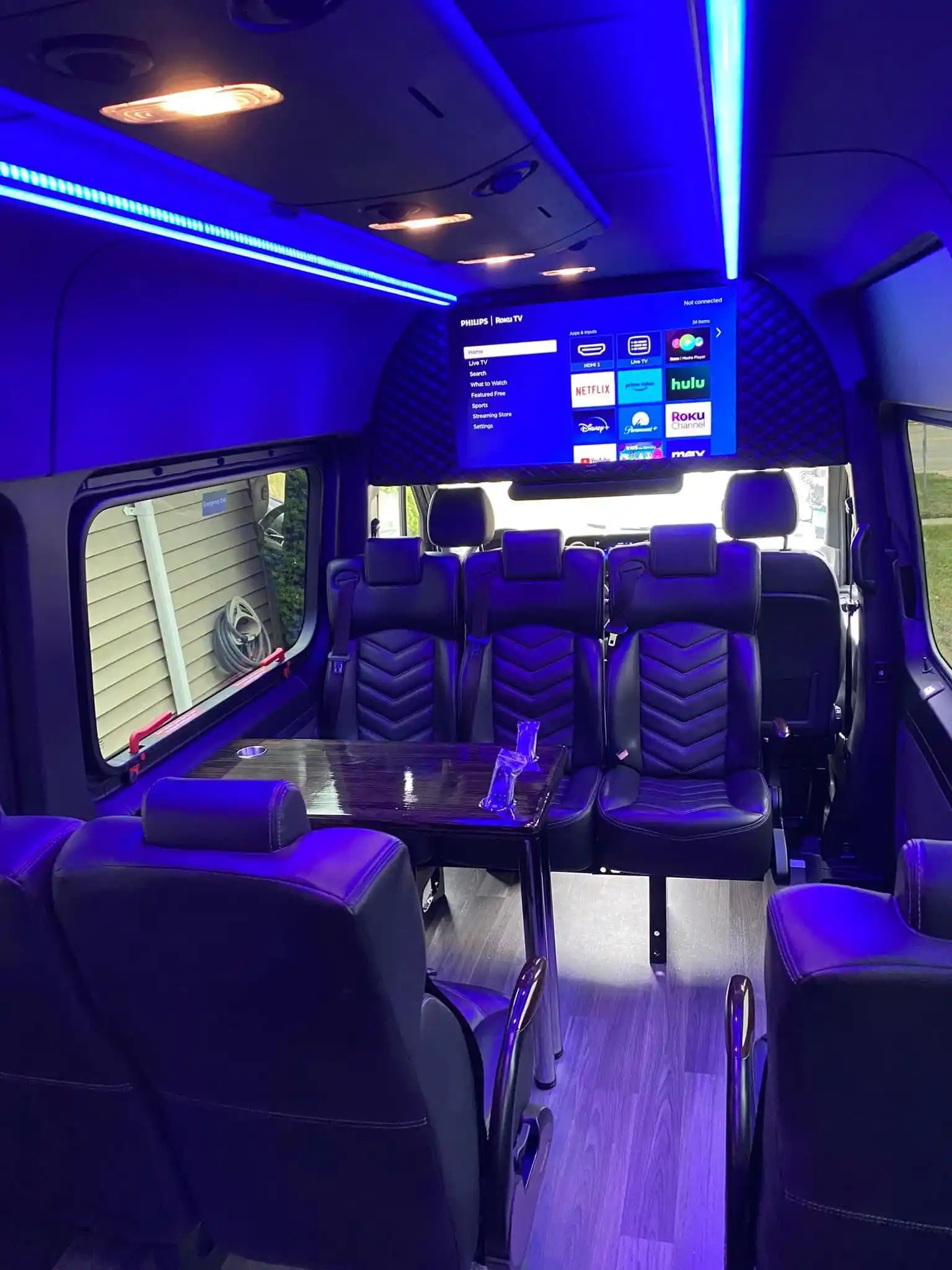 Black luxury van interior with sofa seats, massage and heated chairs, skylights, ambient lighting, mini bar, LCD TV, and speakers.