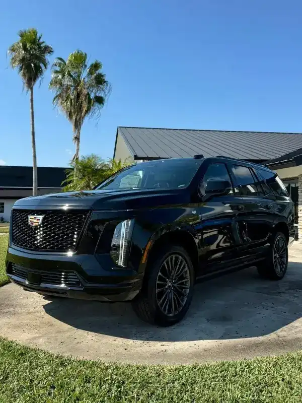 A black luxury Cadillac Escalade parked at a high-end resort entrance, ready to pick up a passenger.